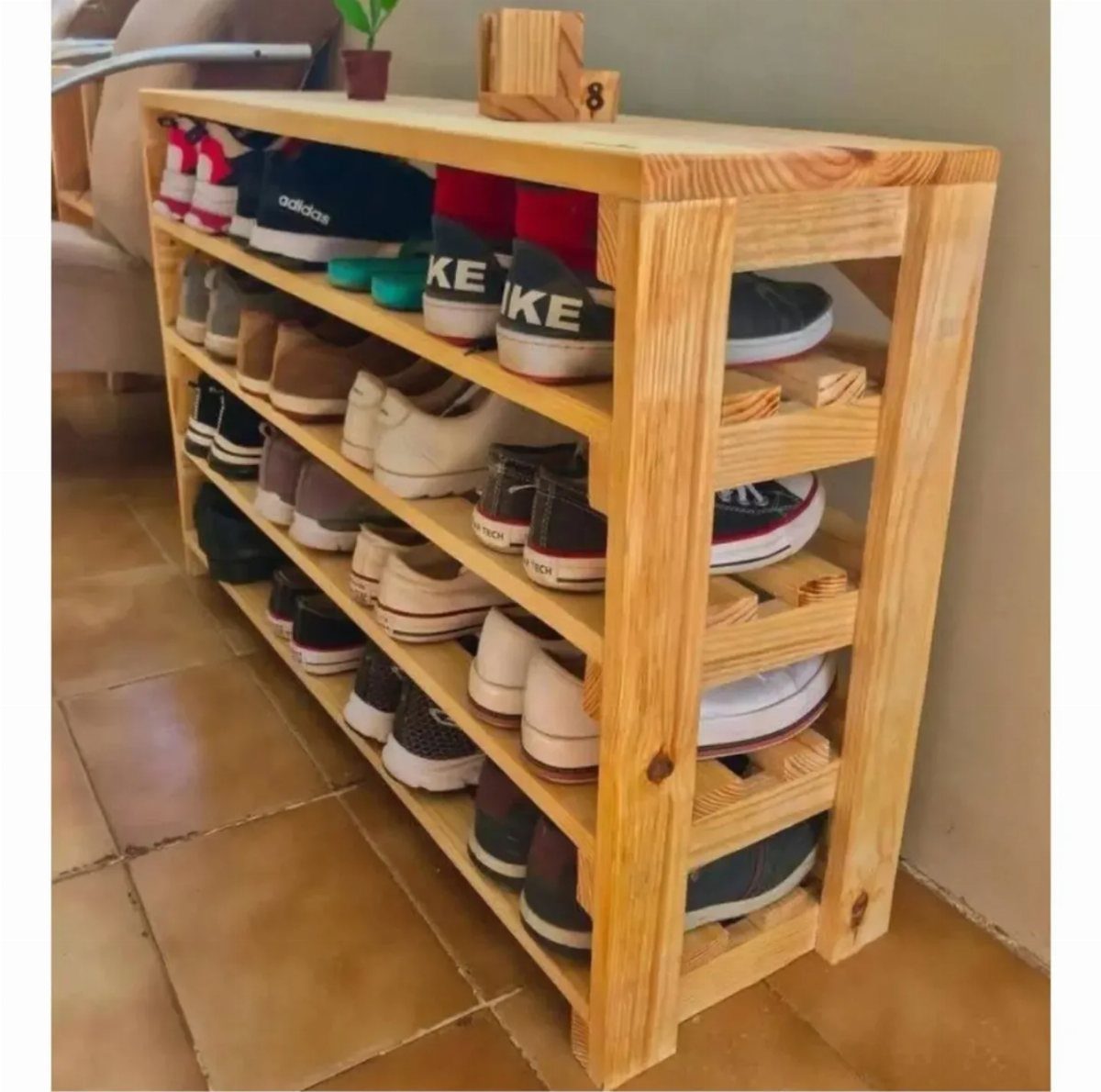 Wooden pallet shoe rack holding multiple pairs of sneakers on a tiled floor.