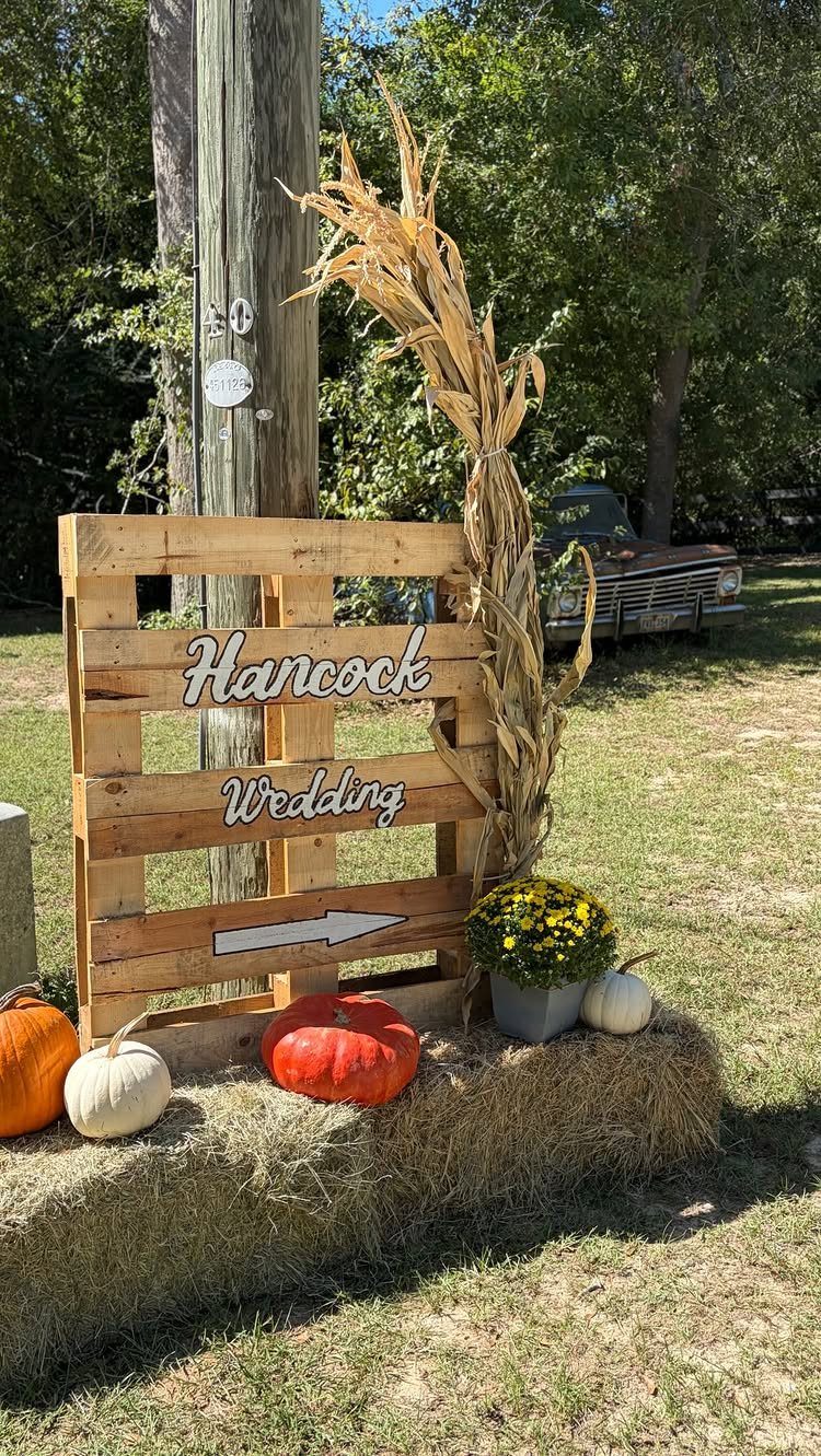 Pallet wood wedding sign with white lettering resting on hay bales with pumpkins.
