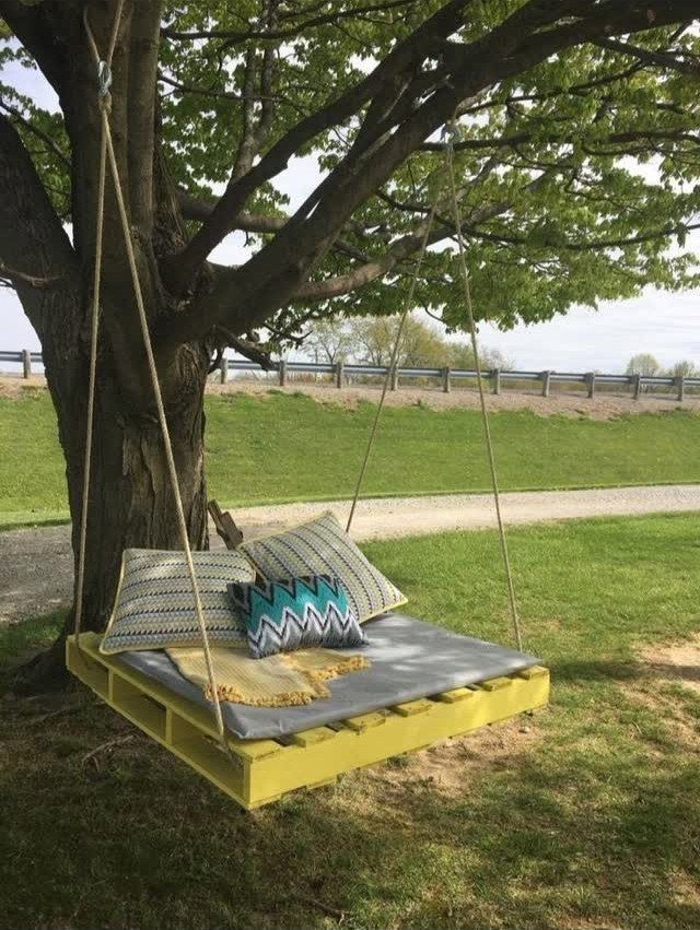Yellow pallet wood swing with cushions hanging from a large leafy tree branch