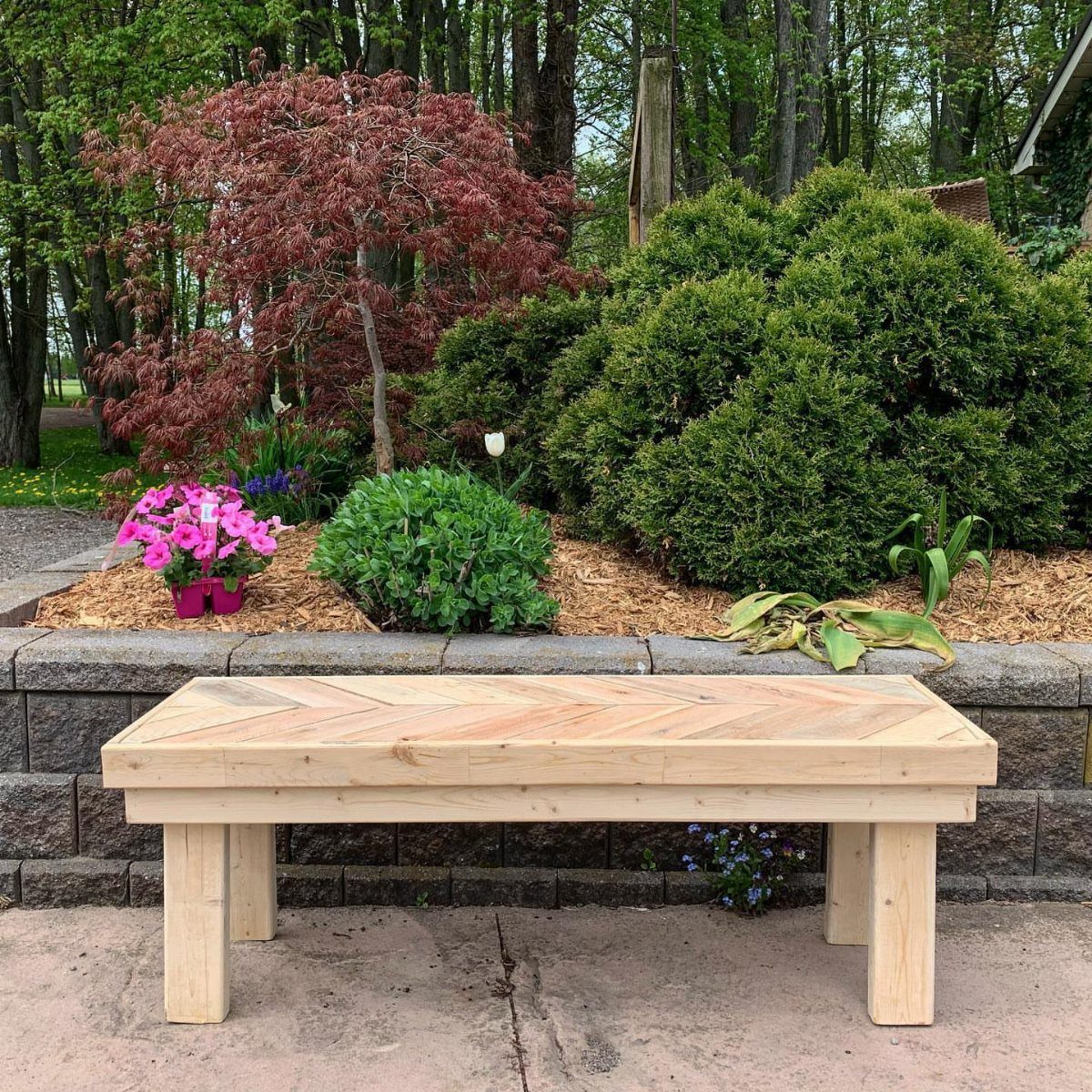 Wooden table with herringbone top set in a lush garden with red maple.