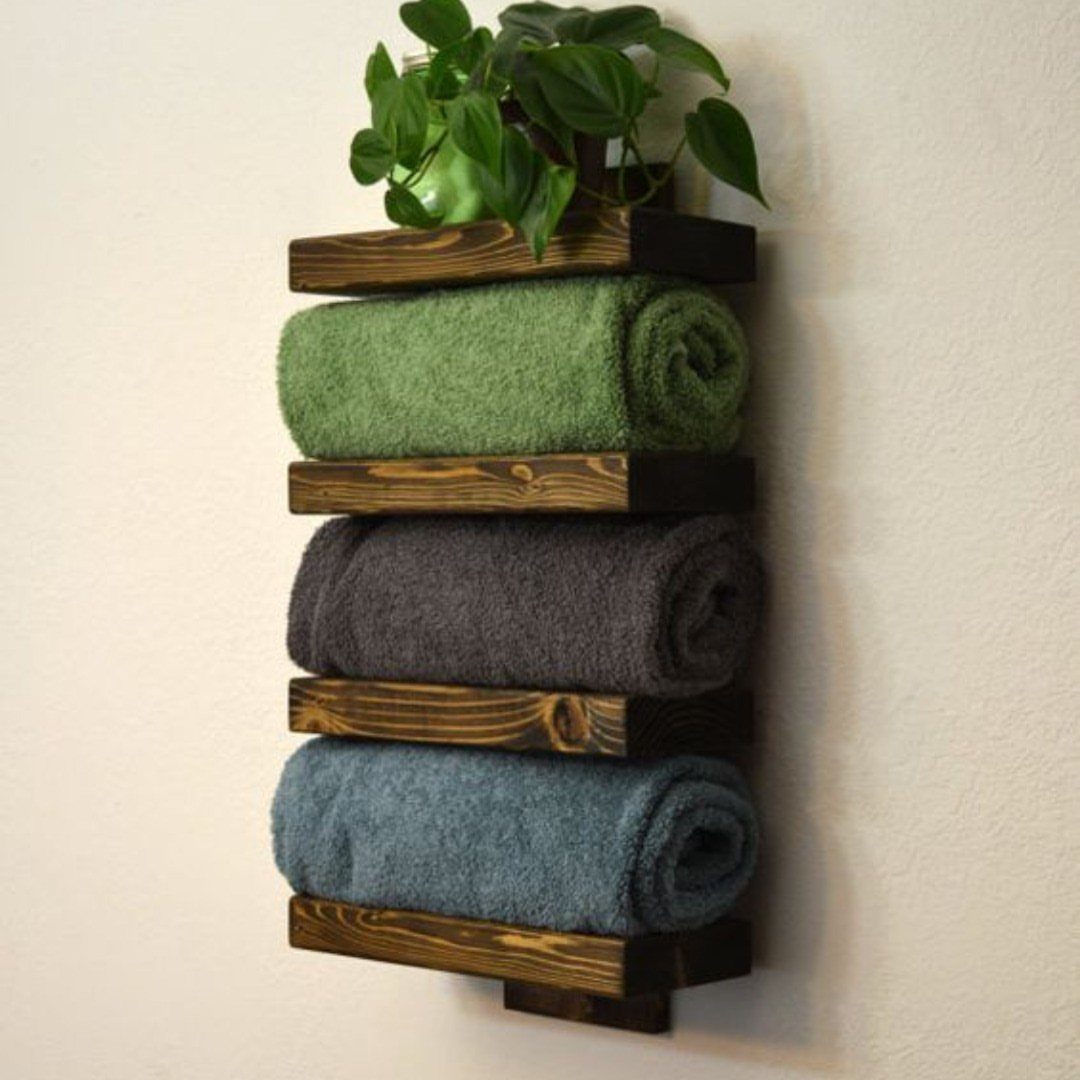 Wooden pallet towel rack with rolled towels and a plant on a white wall