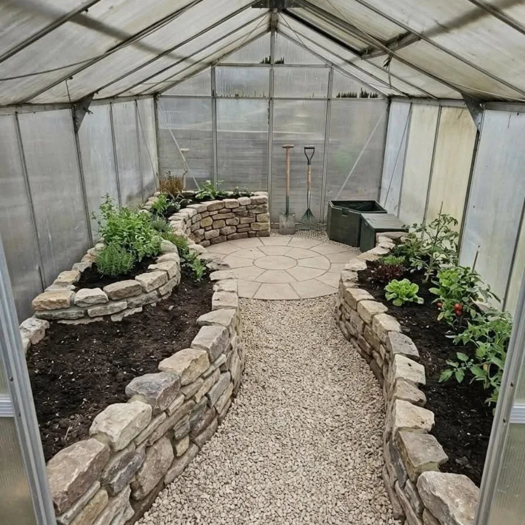 Gravel path and stone patio inside a greenhouse with raised stone garden beds.