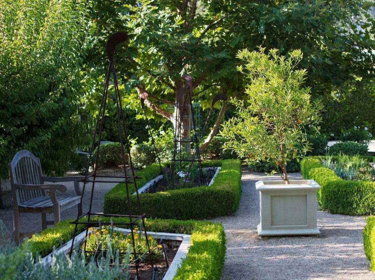 Manicured garden with boxwood hedges, gravel paths, and a white square planter.