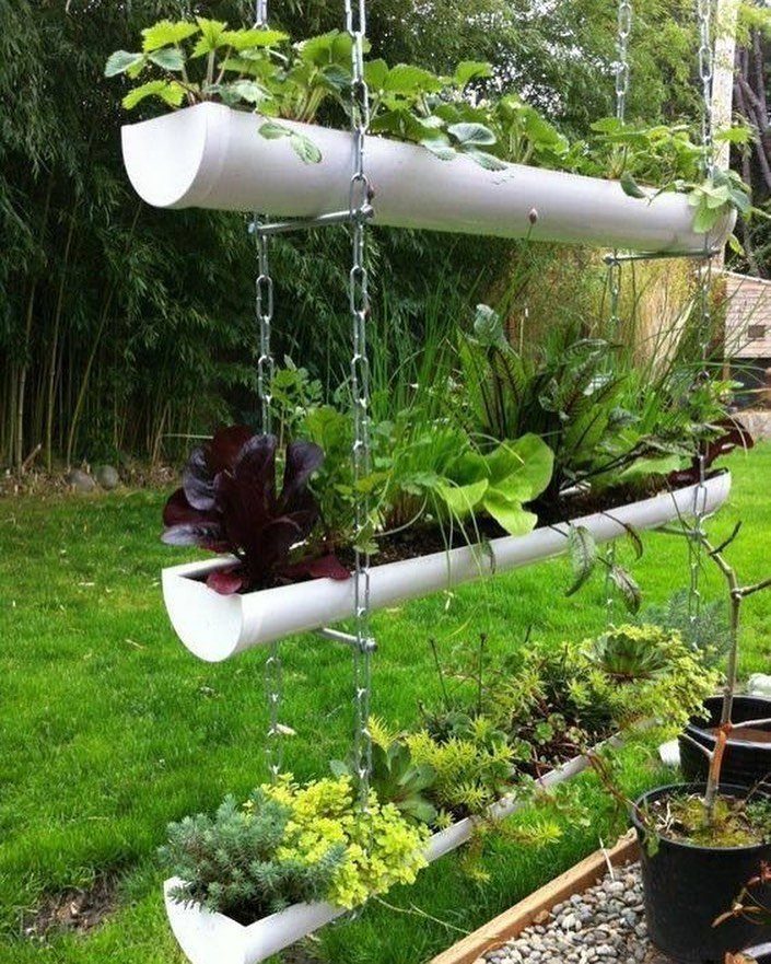 Three white gutter planters hanging vertically with various green and purple foliage plants.