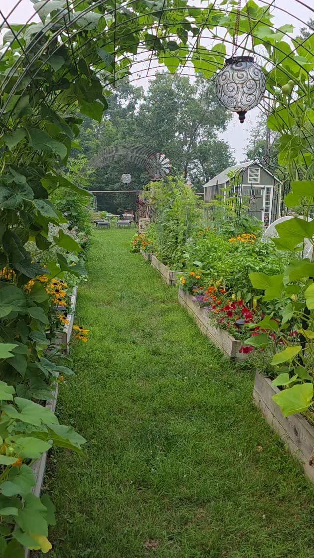 Raised garden beds with mixed vegetables and colorful flowers along a grass path.