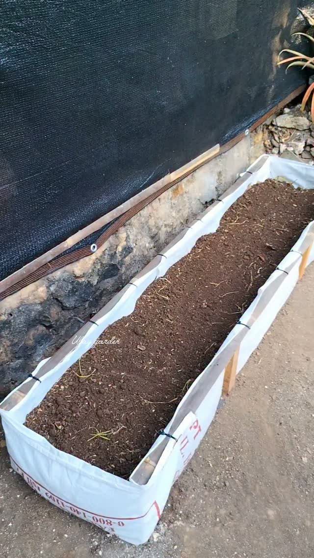 Raised Beds Garden: 25 Ideas from Wood, Metal, and Stone 17 White fabric raised garden bed filled with soil against a stone wall.