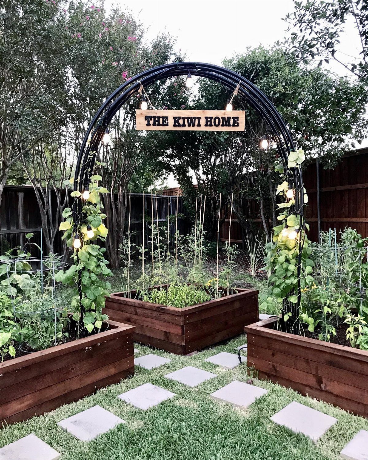 Raised Beds Garden: 25 Ideas from Wood, Metal, and Stone 12 Wooden raised garden beds under a black metal archway with a wooden sign.
