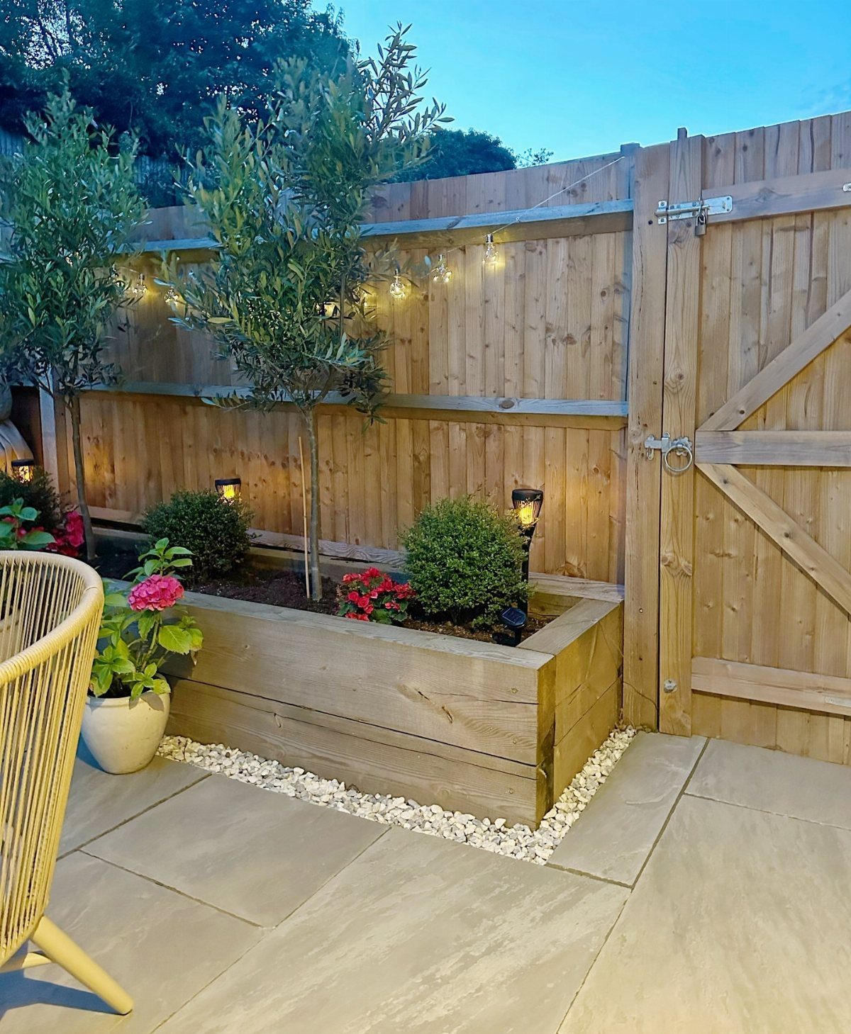 Raised Beds Garden: 25 Ideas from Wood, Metal, and Stone 10 Wooden raised garden bed with string lights and solar lamps against a fence.