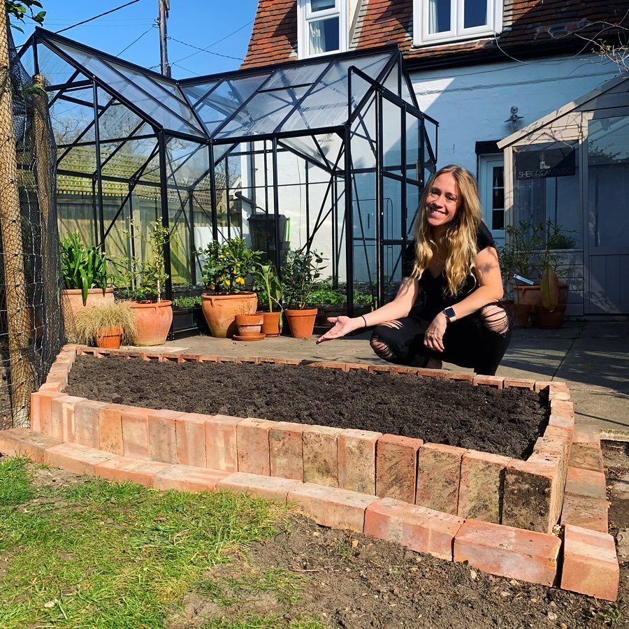 Brick raised garden bed filled with soil with a woman squatting beside it.