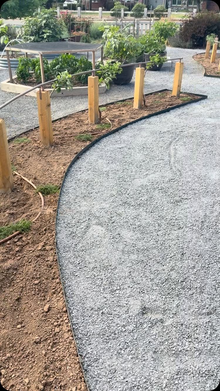 Curved gravel garden path with wooden posts and a galvanized stock tank bed.