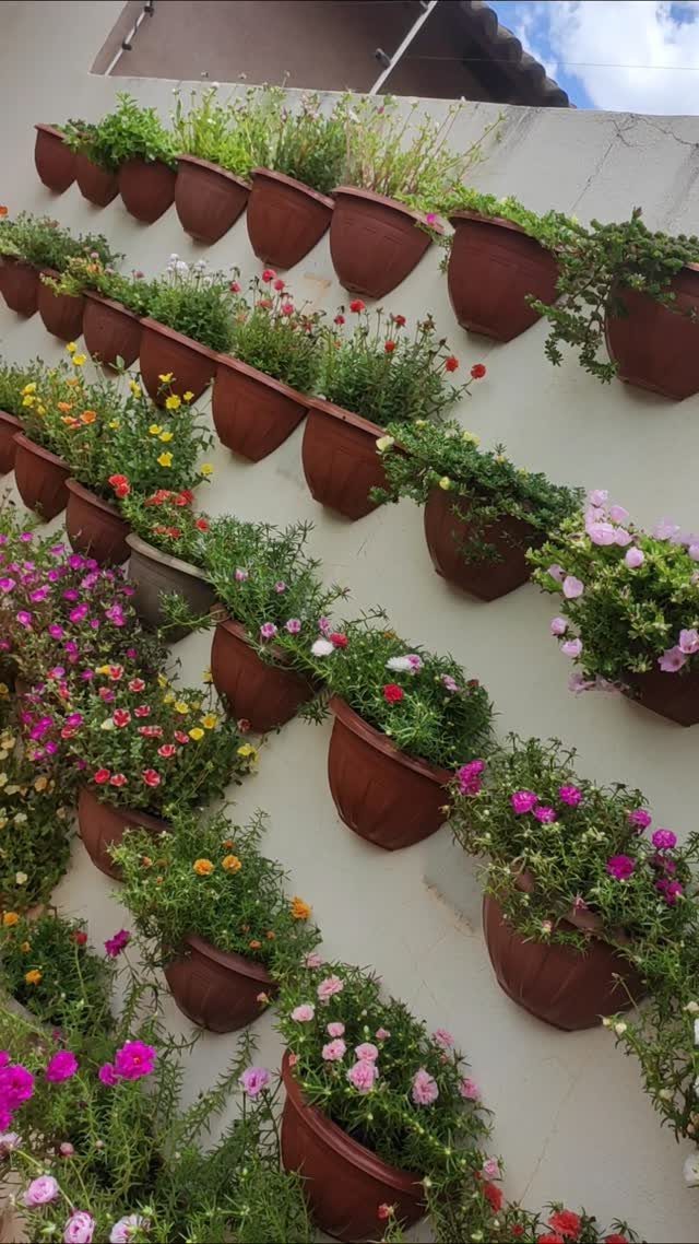 Brown plastic pots with colorful flowers mounted in diagonal rows on a white wall.