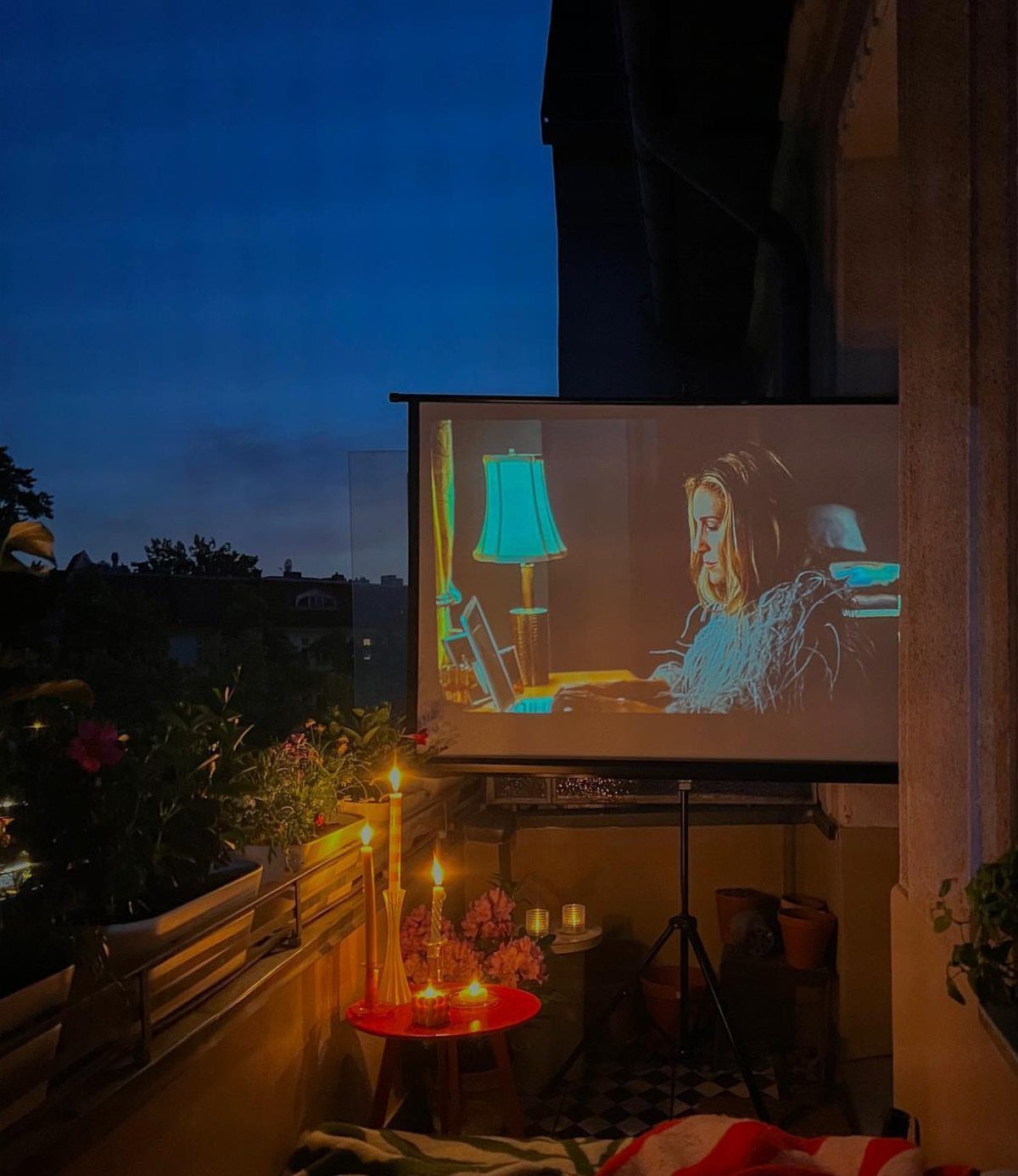 Projector screen showing a movie on a balcony with candles and plants at dusk.