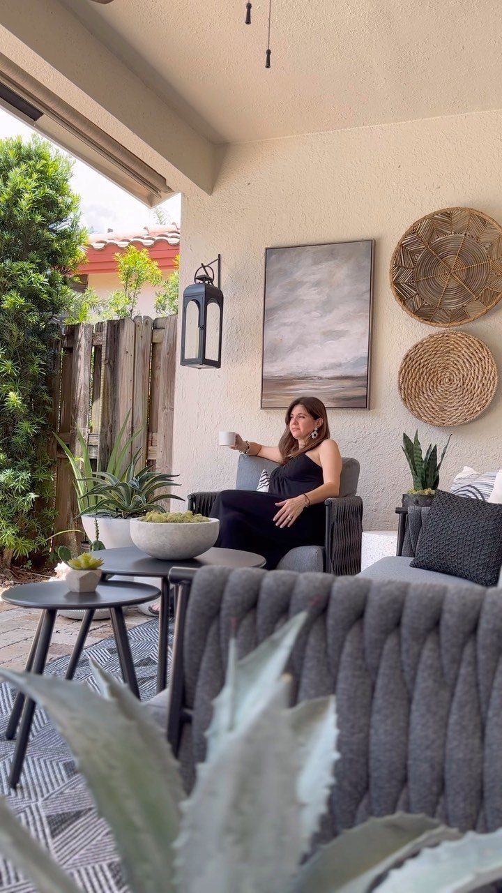 Woman sitting on a patio with a landscape painting and woven baskets on the wall.