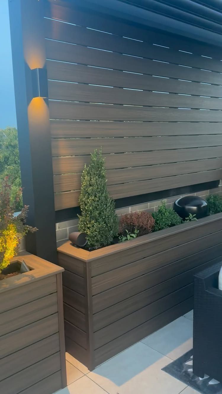 Wooden planter boxes with green shrubs against a slatted privacy wall on a rooftop.