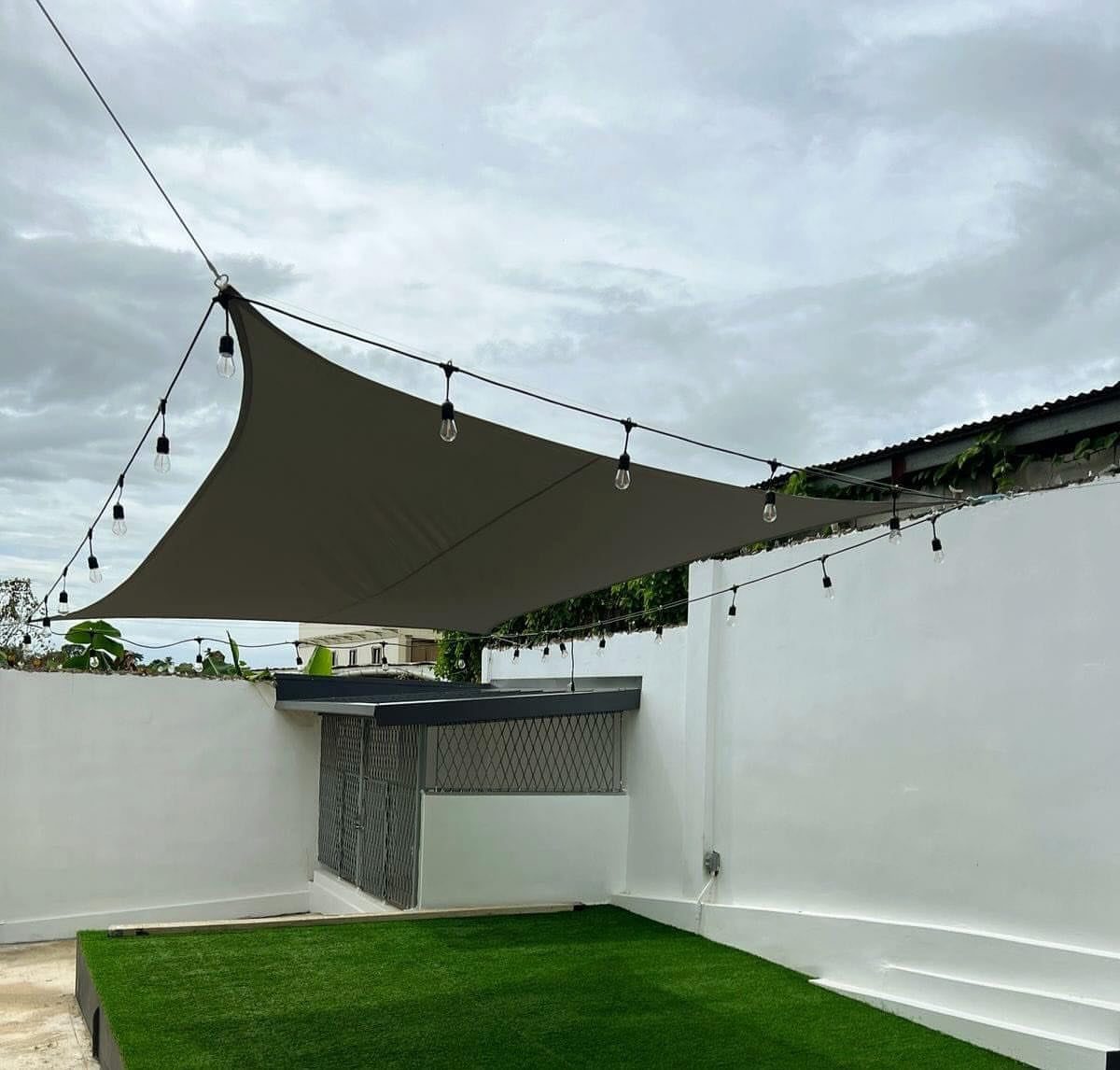 Grey triangular shade sail over a rooftop patio with green grass and string lights.