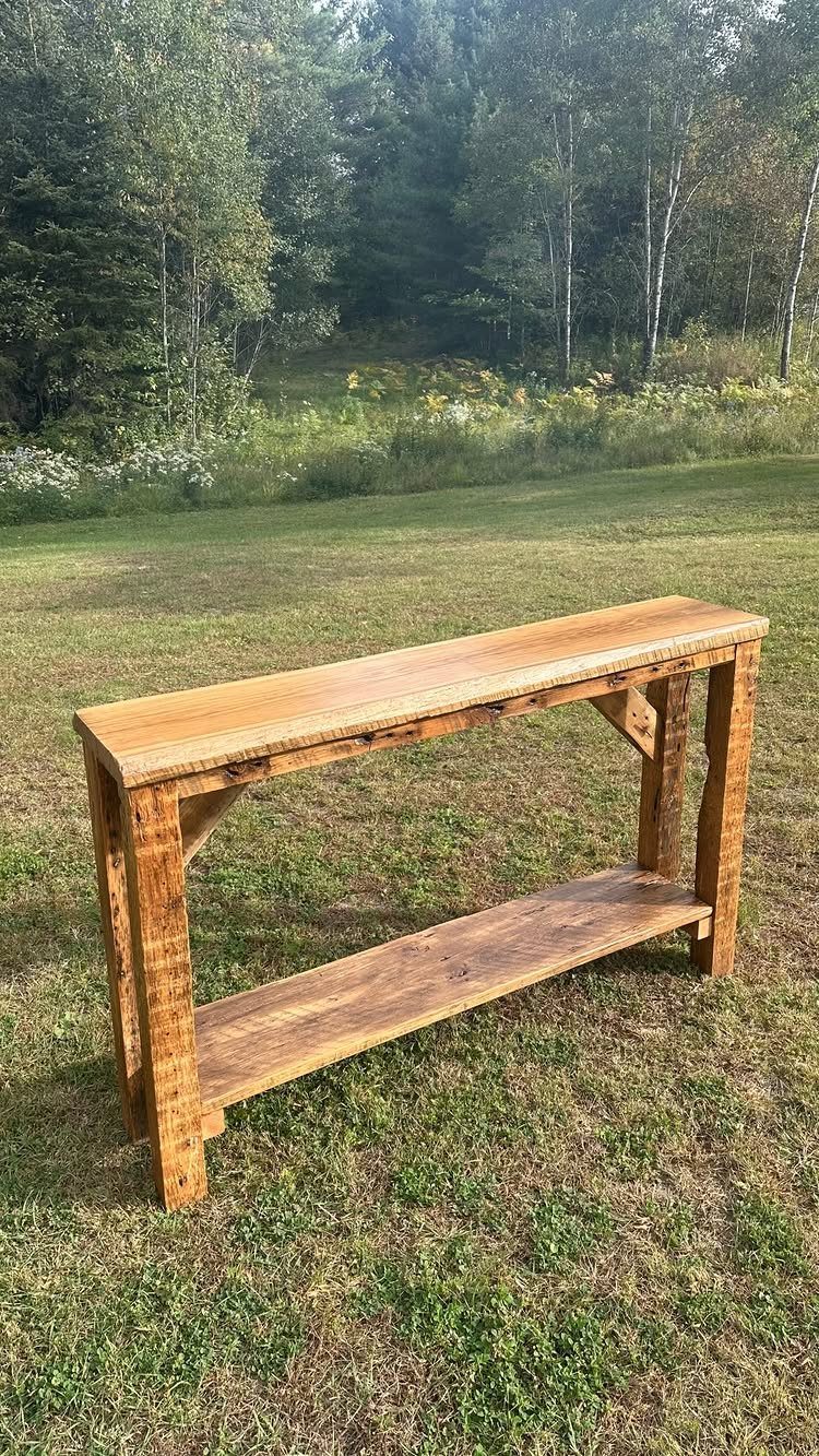 Rustic wood bar-height table with a lower shelf standing on a green grassy lawn.
