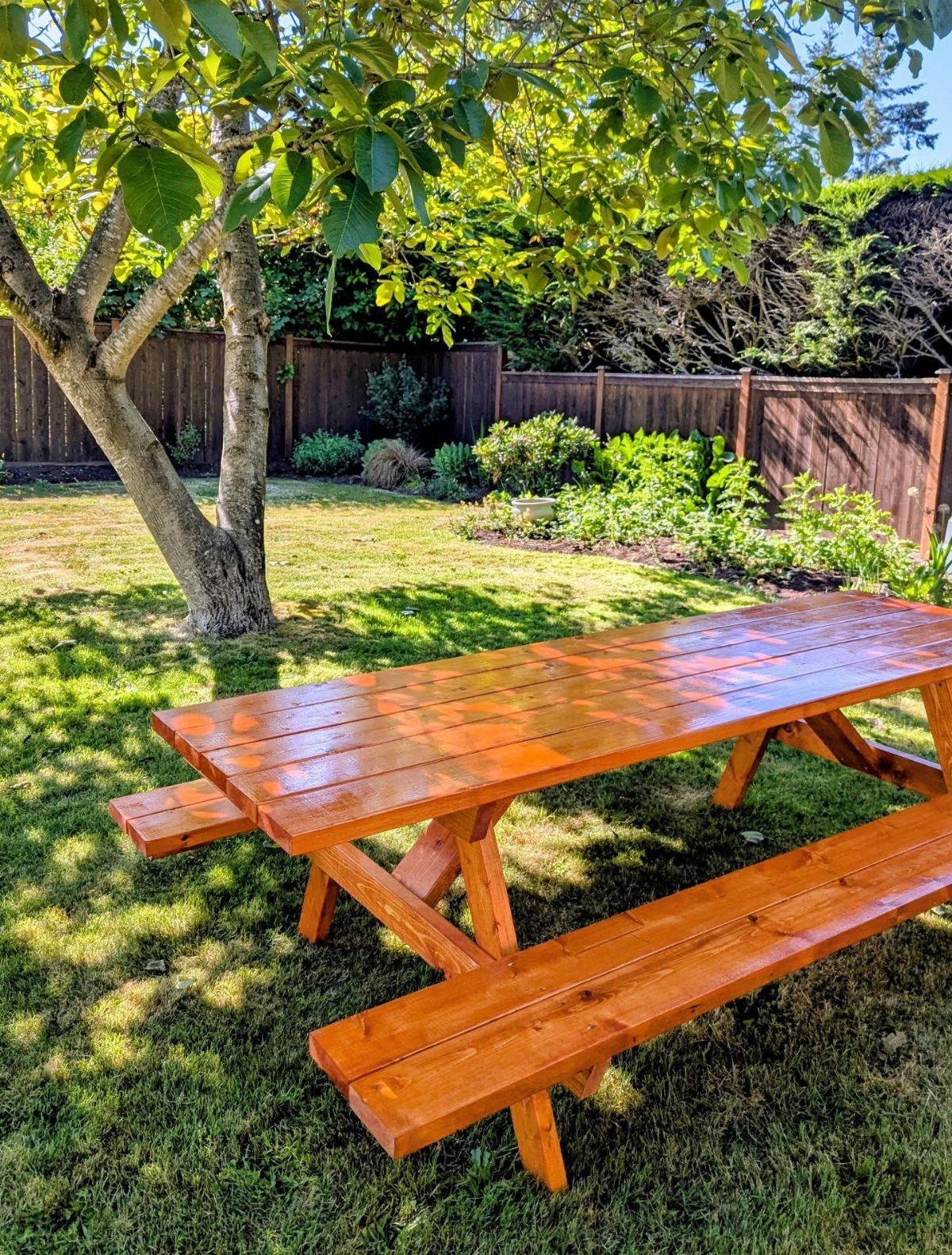 Wooden picnic table with benches on a sunny green lawn under a tree