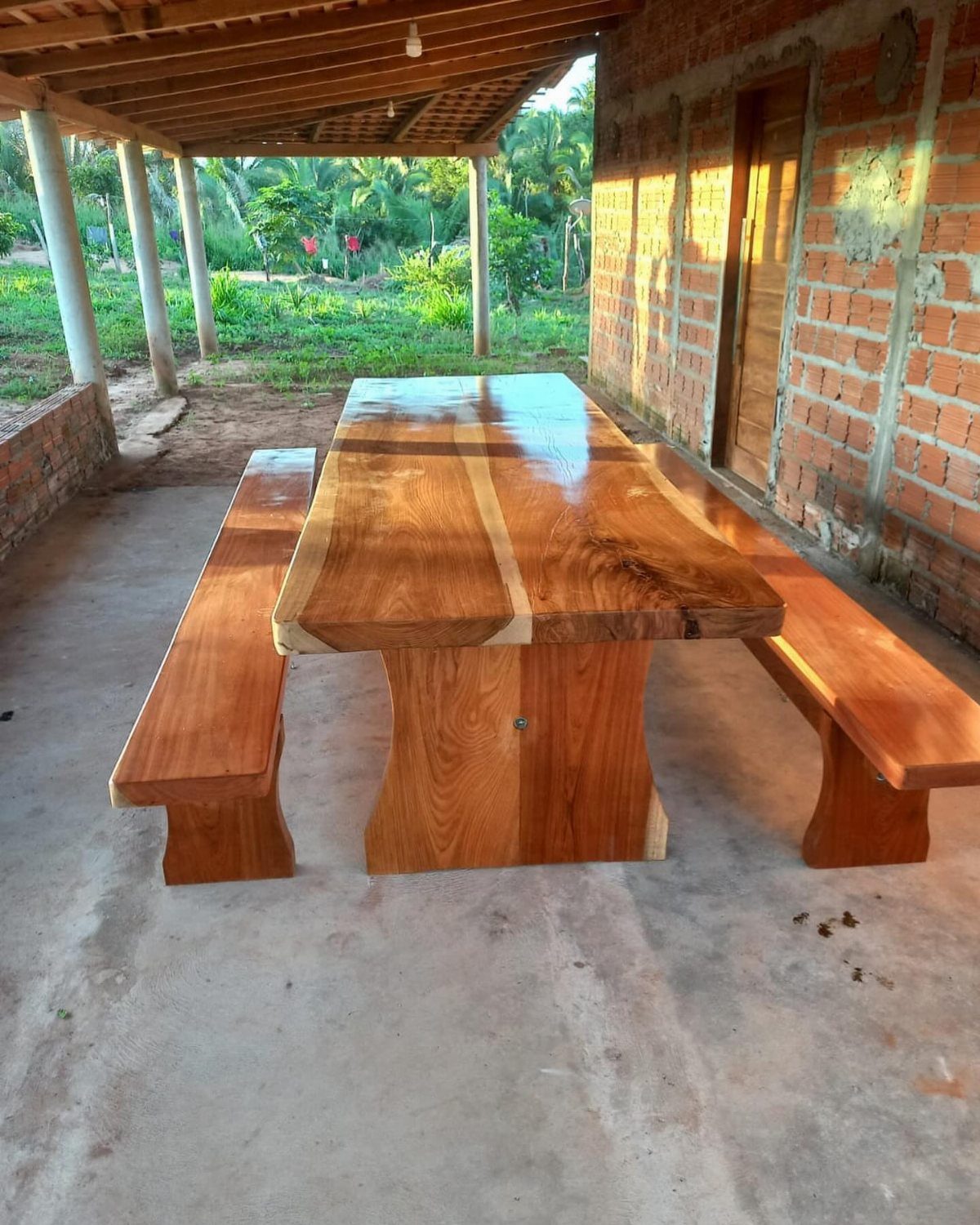 Rectangular polished wood dining table with matching benches on a concrete outdoor patio.