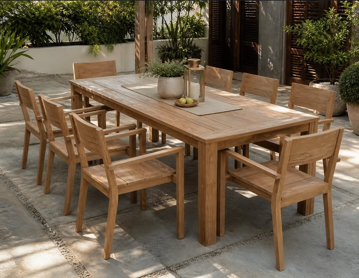 Rectangular teak dining table and matching chairs on a sunny stone patio.