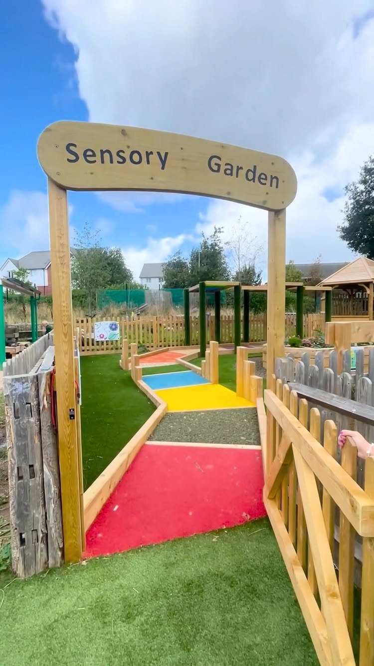 Sensory garden entrance with a wooden sign and a colorful textured walking path.