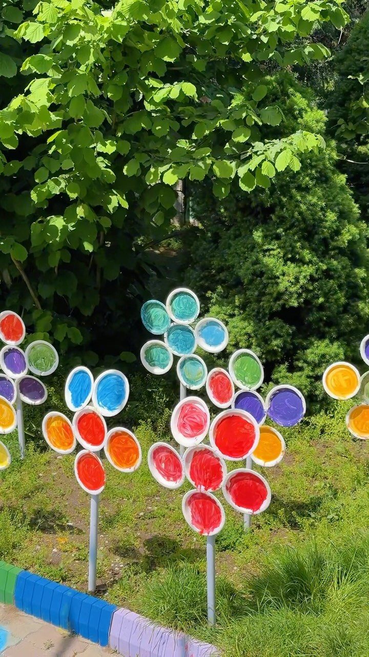 Colorful handmade flower sculptures standing in a lush green garden with dense foliage.