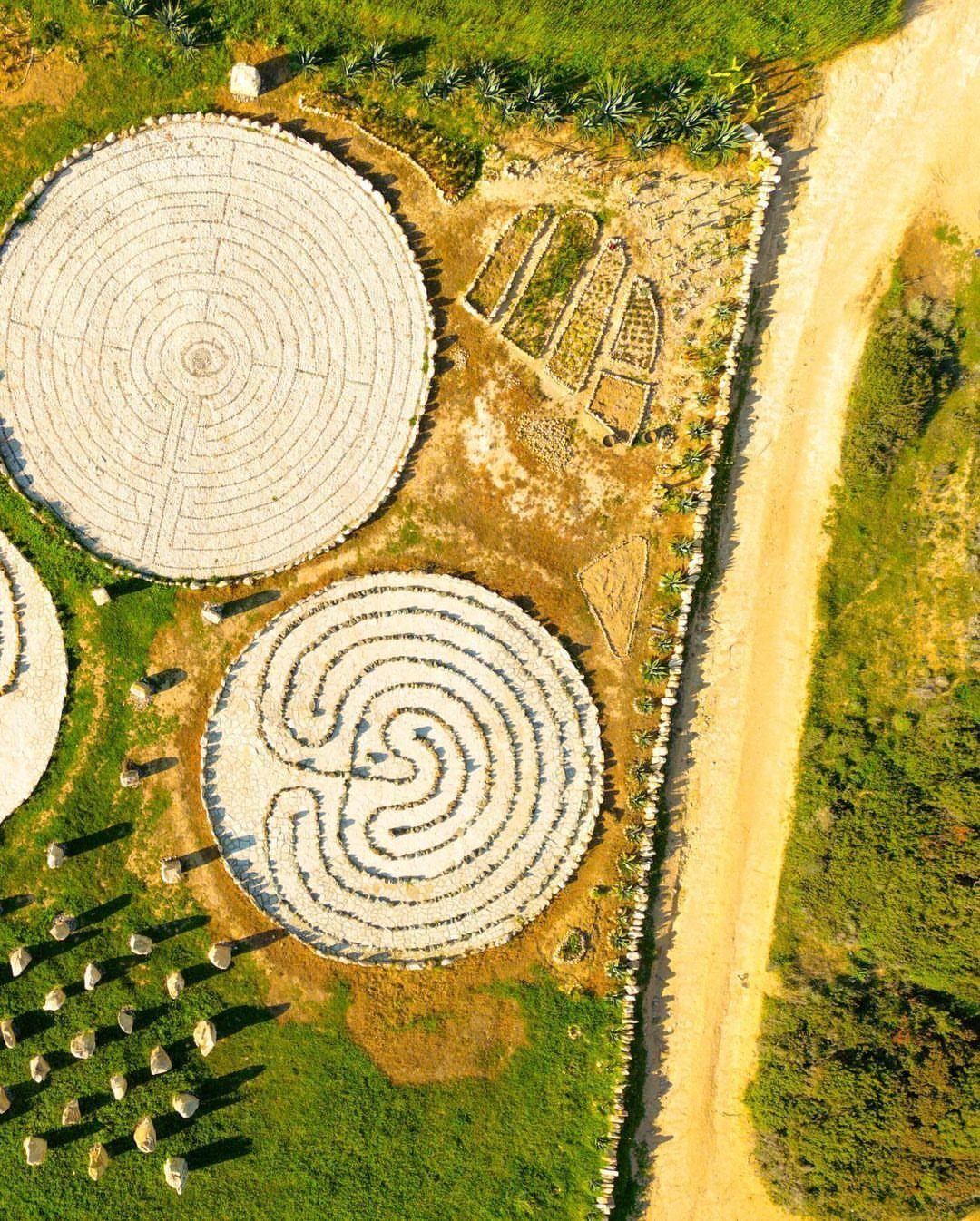 Two circular stone labyrinths and a small garden plot in a green field.