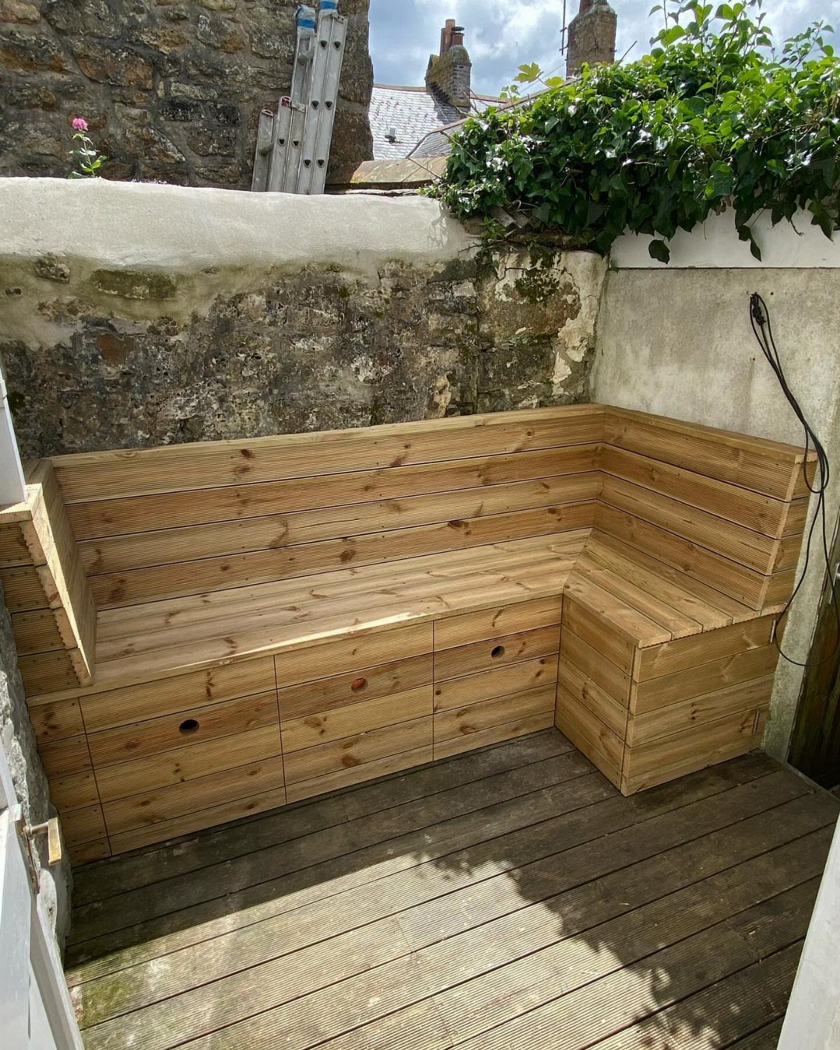 Wooden L-shaped corner bench with storage compartments on a garden deck