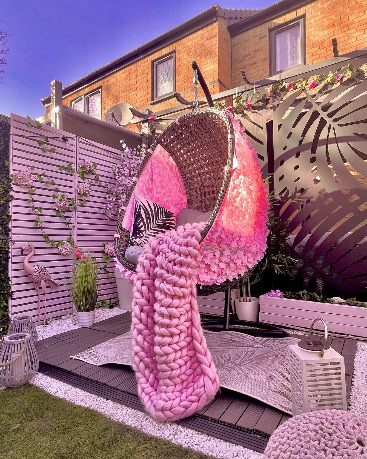 Pink hanging egg chair on a patio with decorative laser-cut garden screens.