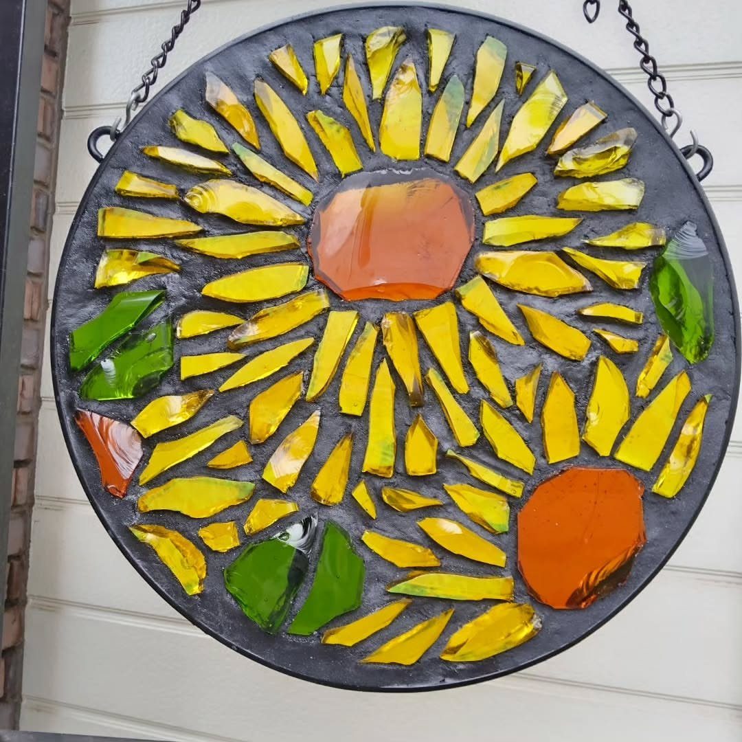 Circular stained-glass sun catcher with yellow and orange glass shards hanging on a wall.