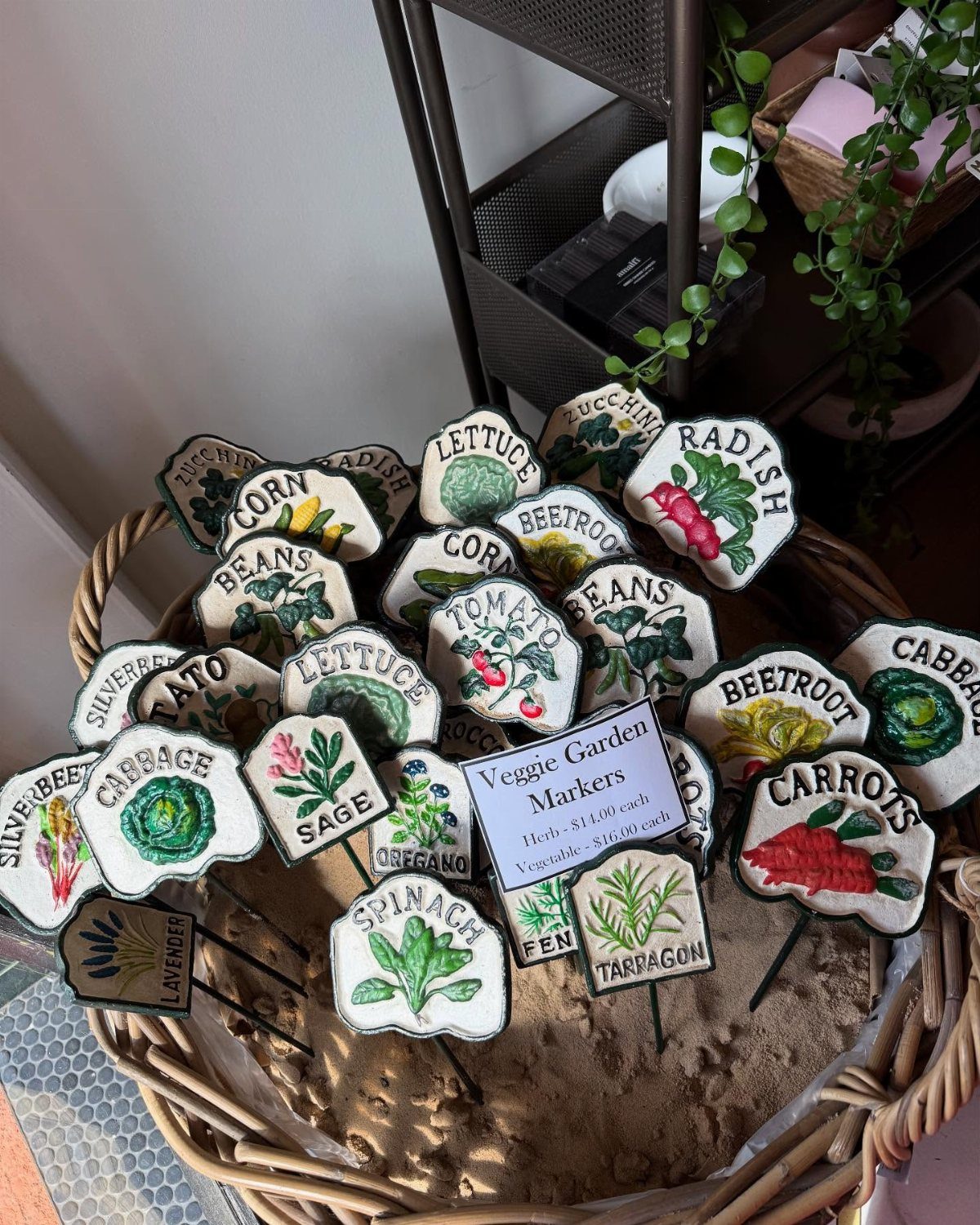 Ceramic plant markers with painted vegetables and names displayed in a wicker basket.