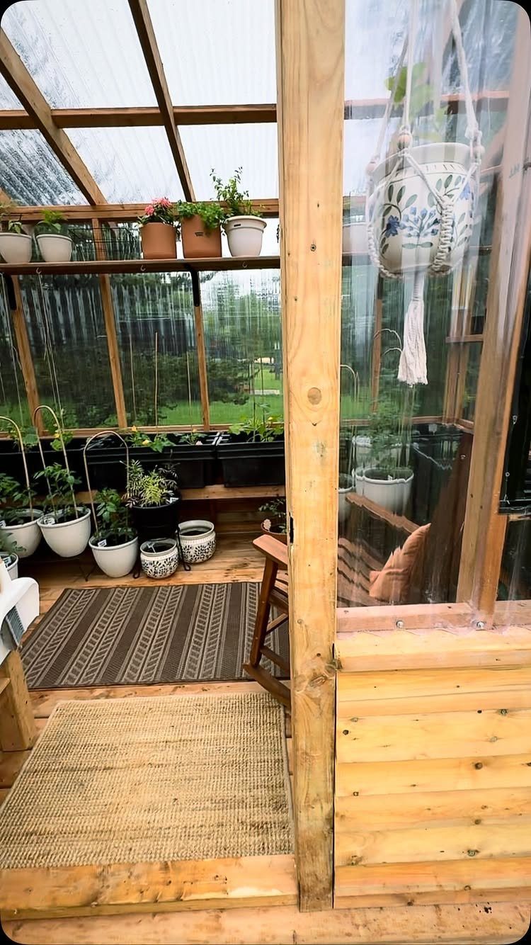 Wooden greenhouse interior with various potted food plants and woven floor rugs.