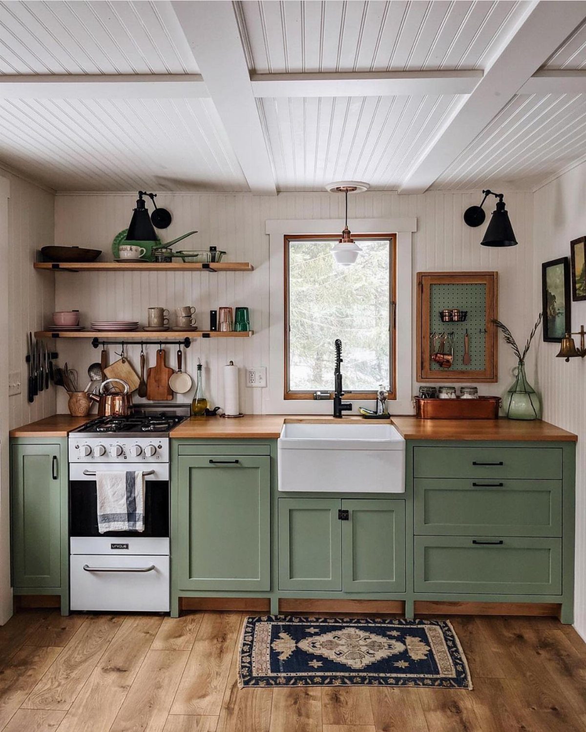 Sage green kitchen cabinets with a white farmhouse sink and white oven stove.