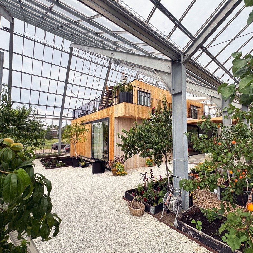 Modern wooden house built inside a large glass and metal frame greenhouse structure.