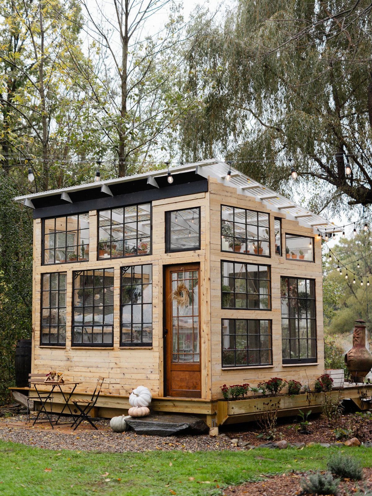 Wooden greenhouse with black window frames and white roof on a garden deck.
