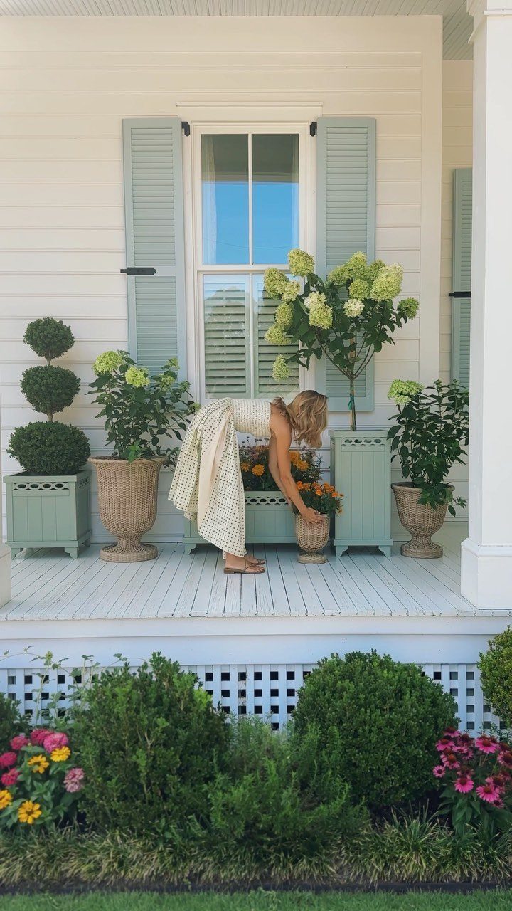 Woman tending to large urns and planters on a white wooden porch.