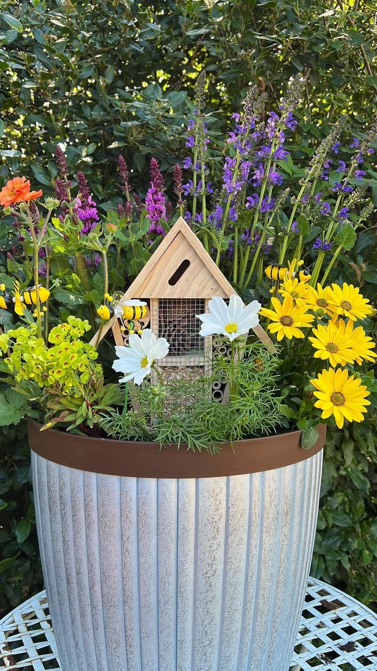 Ribbed metal planter with colorful summer flowers and a small wooden birdhouse.