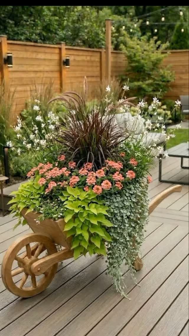Wooden wheelbarrow planter filled with purple grass, pink flowers, and trailing silver foliage.