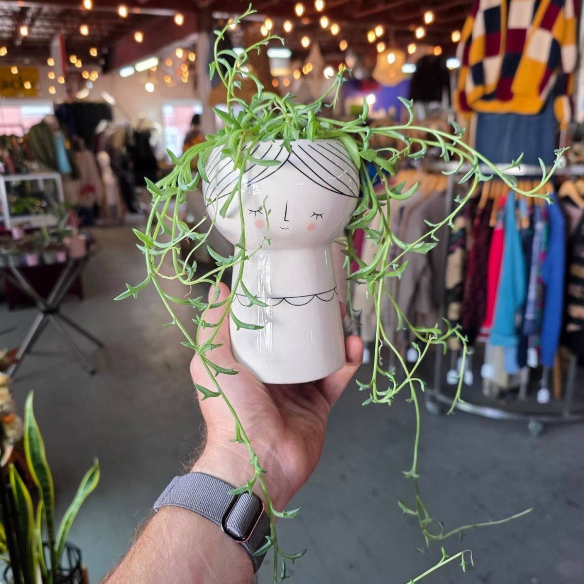 18 Unique Pots for Plants, From Resin Corgis to Copper Flowers 3 White ceramic human head planter with a trailing green plant held by a hand.
