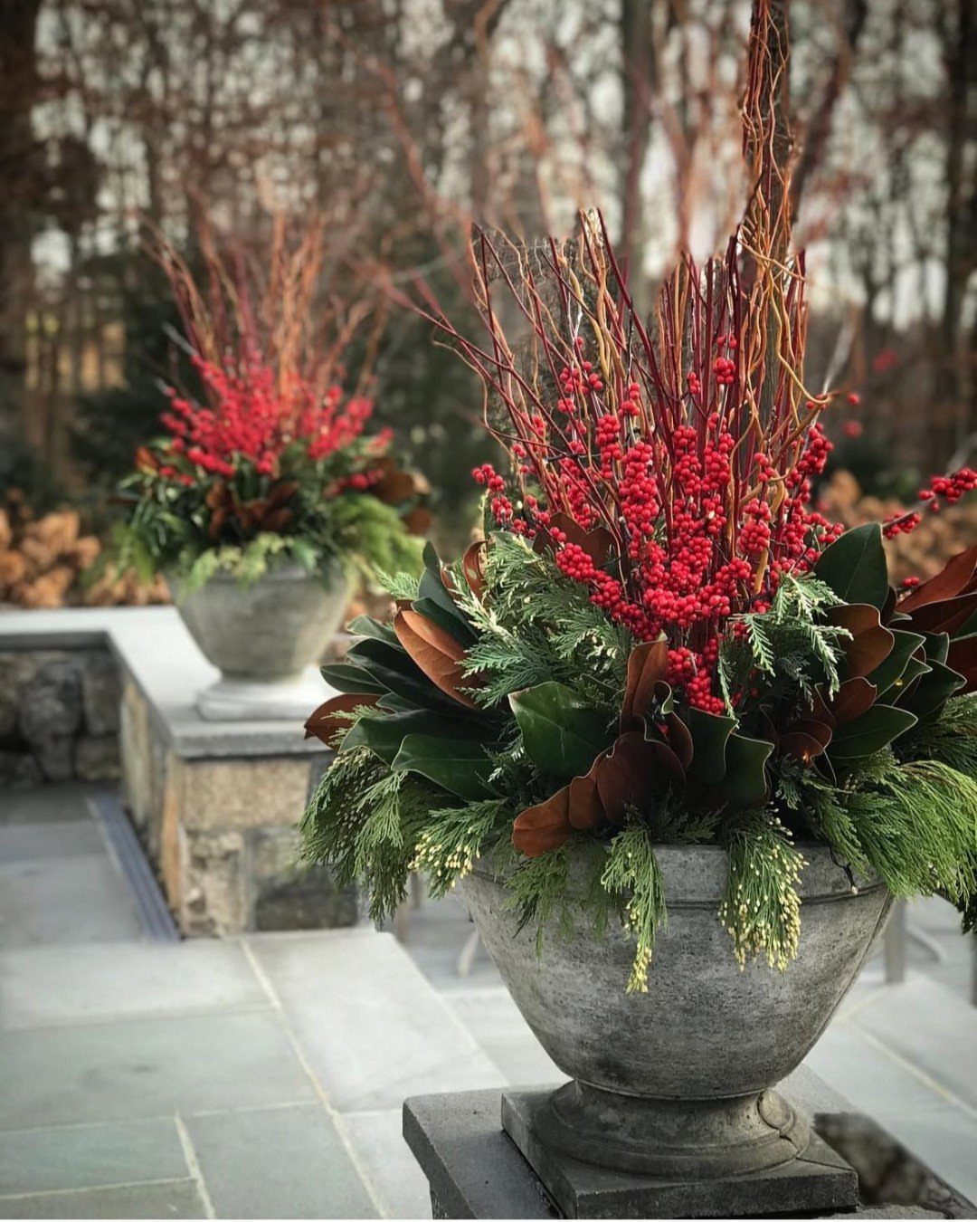 Stone urns filled with red winter berries and evergreen foliage on a patio.